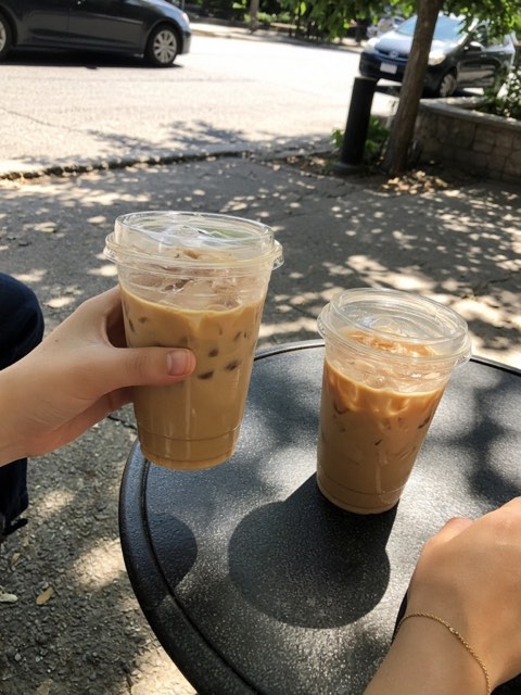 two iced coffees held up in front of a street