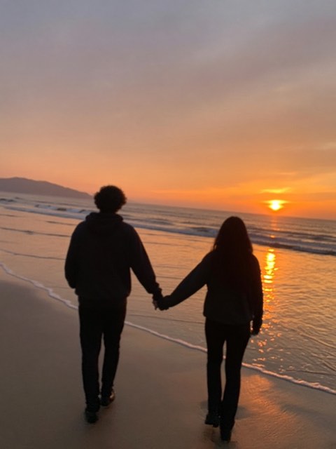 two people holding hands on a beach at sunset