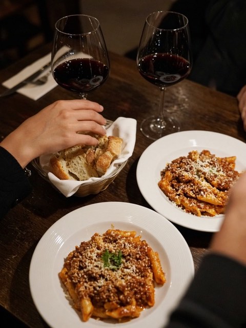 two plates of pasta and glasses of red wine on a restaurant table