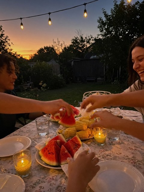 a table outside at dusk with string lights, watermelon and candles